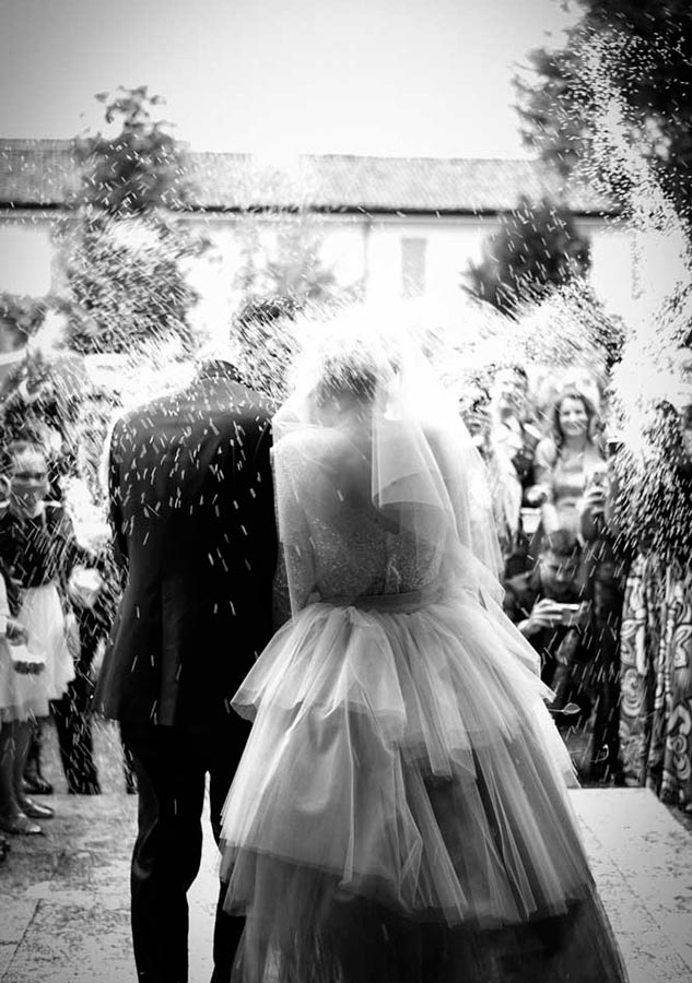 gli sposi all'uscita dalla chiesa sotto la pioggia di riso in bianco e nero
